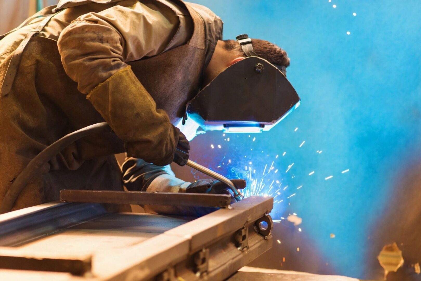 Young man welding in a facility while wearing a safety mask.